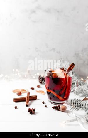 Weihnachtszeit Konzeptfoto. Glastasse oder Becher mit Glühwein auf weißgrauem Tischhintergrund. Girlanden und Lichter, Weihnachtsschmuck, Zimt, Stockfoto