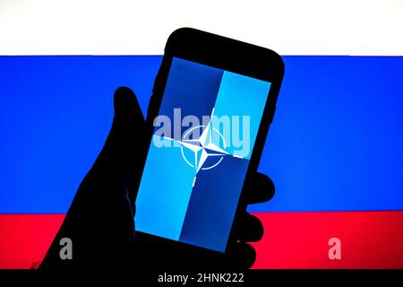 In dieser Abbildung ist eine Flagge der NATO (North Atlantic Treaty Organization) auf einem Smartphone-Bildschirm und die Flagge Russlands im Hintergrund zu sehen. Stockfoto