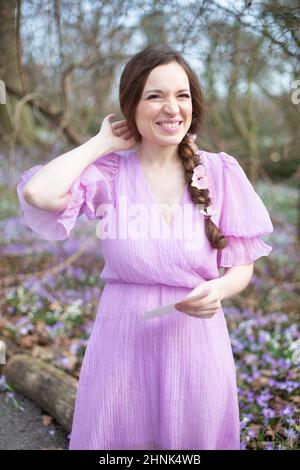 Lächelnde europäische Frau im lila Kleid mit braunen Haaren im Park Stockfoto