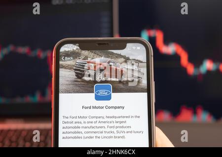 Die Aktienkursrückgang der Ford Motor Company am Handelsmarkt mit einem Balkendiagramm für die Abwärtstrendlinie im Hintergrund. Mann mit Mobiltelefon und Firmenlogo, Februar 2022, San Francisco, USA. Stockfoto