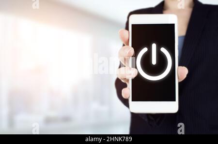 Starten Sie das Geschäftskonzept. Power-Up-Konzept. Weißes Smartphone mit Handgriff und digitaler Hologramm-Taste auf dem virtuellen Bildschirm, das Licht ist unscharf Stockfoto