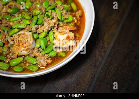 Nahaufnahme Thailändischer, gebratene Stinkbohnen mit Garnelen und würziger Shrimp-Paste-Sauce in einer weißen Schüssel auf einem dunklen Holztisch. Stockfoto