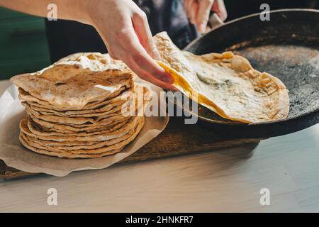 baker's Hände entfernen Pitabrot aus einer gusseisernen Pfanne. Private Mini-Bäckerei Herstellung von Craft Brot und Pita Brot. baker in Schürze in der Küche Stockfoto