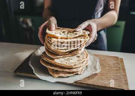 Dünne runde Lavaskuchen werden gestapelt, Hände des Kochens strecken Lavasch nach vorne zum Testen. Spanische Fladenbrot oder armenische Lavaschas aus der Nähe Stockfoto
