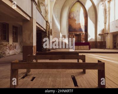 Bänke und Altar in einer verlassenen Kirche. Altes Interieur des religiösen Gebäudes. Kreuz steht in der Ecke Stockfoto