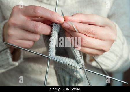 Weibliche Hände halten Stricknadeln und stricken eine Socke. Handgefertigtes und Hobby-Konzept. Nahaufnahme. Stockfoto