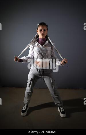 Junge Frau steht und zieht ihre Zöpfe, während sie in einer Studioaufnahme auf die Kamera schaut Stockfoto