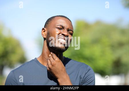 Schwarzer Mann, der sich in einem Park über Rachenschmerzen beschwert Stockfoto