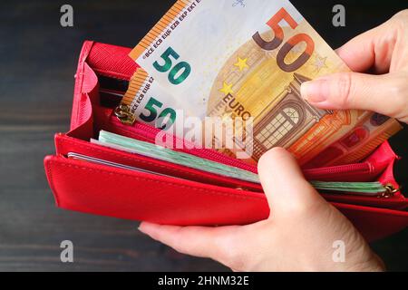 Nahaufnahme der Hand einer Frau, die einen Haufen Euro-Banknoten in einer roten Brieftasche hält Stockfoto