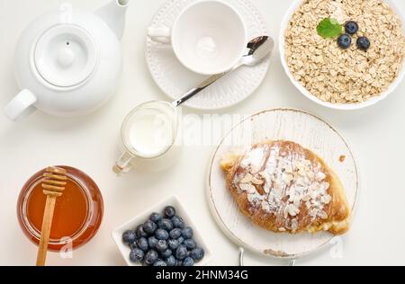 Roher Haferflocken in weißer Keramikplatte, Heidelbeere, Honig auf weißem Tisch, Frühstück. Draufsicht Stockfoto