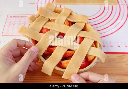 Hand weben Stücke des geschnittenen Teigs auf Kuchenplatte für Gitter Oberkruste eines Apfelkuchen Stockfoto