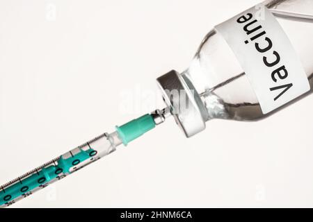 Glasfläschchen mit Etikett-Impfstoff auf weißem Hintergrund, grüne hypodermische Spritzennadel innen - Impfkonzept. Stockfoto