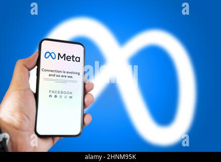 Hand hält ein Telefon mit der Meta Mobile App auf dem Bildschirm und das Logo im Hintergrund verschwommen Stockfoto
