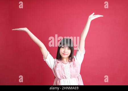 Das Teenie-Asiatin mit niedlichem japanischem Kostüm steht auf dem roten Hintergrund. Stockfoto