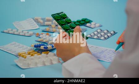 Arzt schreibt ein Rezept mit einer Pillenblase. Stapel von Pillen in Blisterpackungen auf blauem Hintergrund. Stockfoto