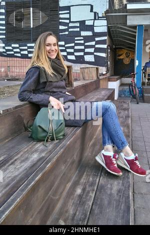 Eine junge Frau sitzt auf einer hölzernen Stufe und lächelt und schaut in die Kamera Stockfoto