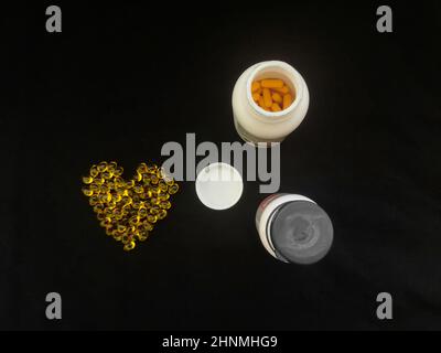 Gelbe transparente herzförmige Kapseln und Gläser mit Pillen auf schwarzem Hintergrund Stockfoto