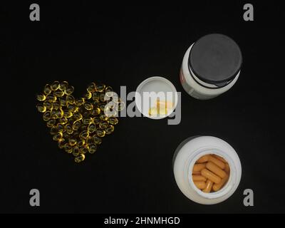 Zwei Dosen Medizin, eine Handvoll gelber, transparenter herzförmiger Kapseln auf schwarzem Hintergrund Stockfoto