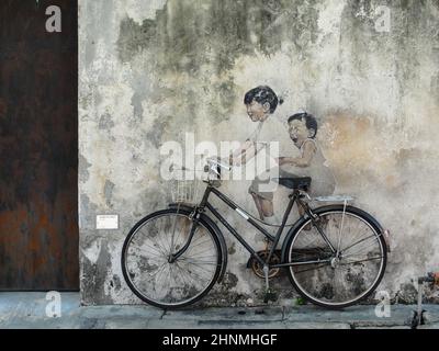 Kleine Kinder auf einem Bicycl. Straßenkunst an der Wand des litauischen Künstlers Ernest Zacharevic. George Town, Penang, Malaysia Stockfoto