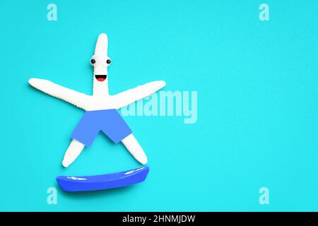 Niedliche Seesterne Charakter Reiten ein Spielzeug Surfbrett isoliert auf einem hellblauen Hintergrund. Kreatives Konzept für aktiven Urlaub. Stockfoto
