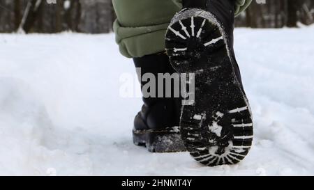 Weibliche Beine in schwarzen Stiefeln, Winterspaziergang im Schnee. Aktive Frau, die im Winterwald von der Kamera wegläuft. Konzentriere dich auf deine Beine. Schönes weißes Winterwetter mit frischem Schneefall. Stockfoto