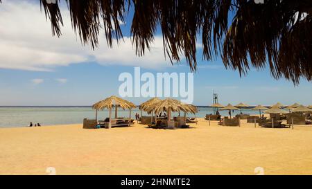 Küste mit Strohschirmen an einem Sandstrand. Seascape am Strand am Ende der Weihnachtszeit. Ein toller Ort zum Entspannen am Roten Meer in Sharm El Sheikh, Ägypten. Stockfoto