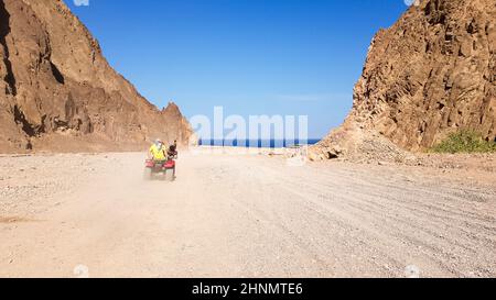 Wüste in Ägypten. Felsige Sandhügel. Ein einsame Tourist auf einem ATV in der Wüste vor dem Hintergrund des blauen Himmels und der Berge läuft in Richtung des Roten Meeres. Landschaft in der Wüste. Stockfoto