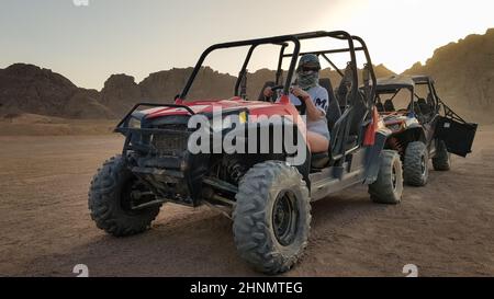 Ägypten, Sharm El Sheikh - 10. Oktober 2020. Aktive Frau, die ein ATV auf einer unbefestigten Straße in der Wüste vor dem Hintergrund der felsigen sandigen Berge im Sonnenuntergang fährt. Stockfoto