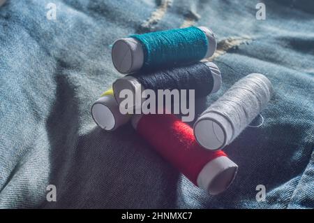 Rollen mit bunten Nähfäden mit Jeans im Hintergrund, Nähkonzept, kopieren Raum in Teilen des Bildes. Stockfoto