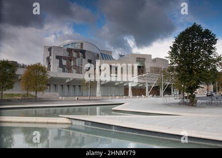 Reflektierende Pools vor dem schottischen Parlamentsgebäude in Edinburgh mit blauem Himmel und Sturmwolken, die sich abzeichnen Stockfoto