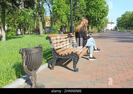 Junges Mädchen nachdenklich Blick auf Smartphone, während auf der Bank im Stadtpark sitzen Stockfoto