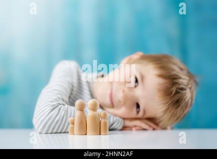 Lächelndes Kind mit Holzfiguren der Familie auf blauem Hintergrund. Konzept der Adoption und Elternschaft. Stockfoto