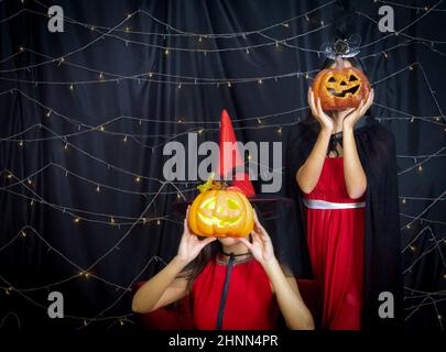 Zwei Frauen in rotem Kleid halten Kürbis in ein Gesicht vor geschnitzt. Atmosphäre in der Halloween Party mit blinkenden Lichtern geschmückt. Stockfoto