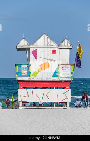 Die Menschen genießen South Beach in Miami Beach und sitzen vor dem farbenfrohen Rettungsschwimmerturm Stockfoto