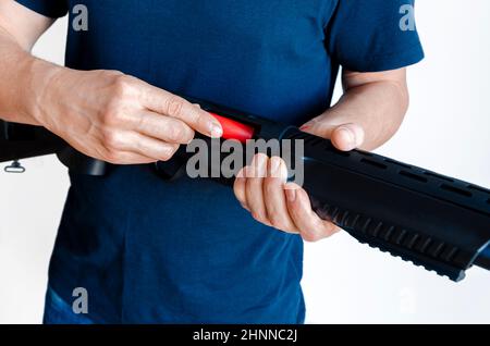 Der Mann lädt die Schrotflinte mit Patronen. Laden einer Glattbore-Waffe der Pumpe. Nahaufnahme. Stockfoto