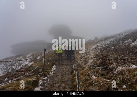 KARPACZ, POLEN - 16. OKTOBER 2021: Touristen besteigen den beliebten polnischen Berggipfel Sniezka im Riesengebirge bei bewölktem Wetter. Im Hintergrund das Gebäude des meteorologischen Observatoriums. Stockfoto