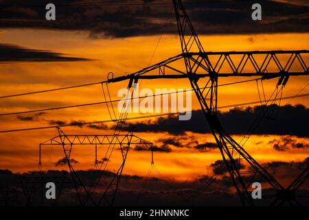 Regenwolken während des wundervollen Sonnenuntergangs schaffen dramatischen Abendhimmel über der Stromleitung im Feld Stockfoto