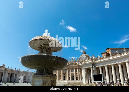 Die Leute auf dem Petersplatz im Vatikan stehen Schlange, um die Basilika mit Brunnen und Blick auf die Kolonnaden zu betreten. Stockfoto