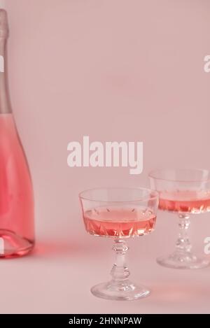 Zwei Kristallgläser und eine Flasche Rosé-Sekt oder Champagner auf pastellrosa Hintergrund. Urlaubskonzept. Minimale kreative Komposition mit Kopierplatz. Stockfoto