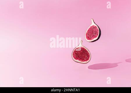 Frische leckere Feigenfrucht halbiert Levitation mit Schatten auf rosa Hintergrund. Zwei Querschnitte von Feige fallen herunter oder fliegen. Veganes Wüstenkonzept. Schatten von Stockfoto