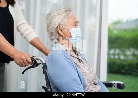 Helfen Sie asiatischen älteren oder älteren Frau im Rollstuhl sitzen und tragen eine Gesichtsmaske zum Schutz der Sicherheitsinfektion Covid-19 Coronavirus. Stockfoto