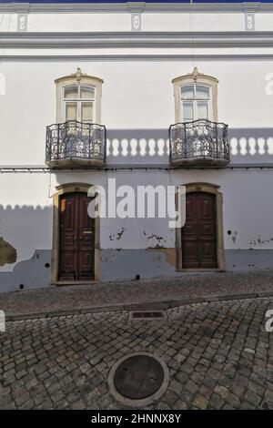 Die schattenspendende, weiß getünchte Fassade des neoklassizistischen Stadthauses besteht aus Metallgeländer, Balkonen und Holztüren. Tavira-Portugal-118 Stockfoto