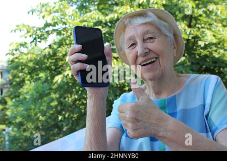 Freudige reife Dame zeigt ein Telefon isoliert auf Natur Hintergrund Stockfoto