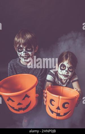 Zwei Kinder mit Totenkopf Make-up halten Kürbis Eimer an Halloween. Stockfoto