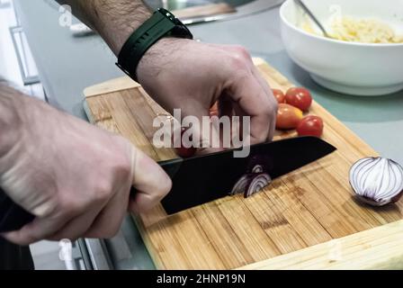 Die Hände des Mannes schneiden Zwiebeln auf einem Holzbrett in der Küche Stockfoto