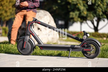 Gefaltet Elektroroller auf Betonpflaster, junge Mann Beine im Hintergrund Stockfoto