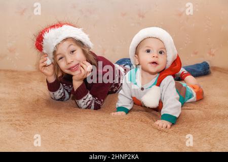 Porträt eines kleinen lächelnden Mädchens und Jungen in Pullovern und Weihnachtsmannmützen. Porträt auf beigefarbenem Hintergrund Stockfoto