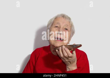 Charmante ältere Frau mit Spracherkennungsfunktion auf dem Handy. Stockfoto