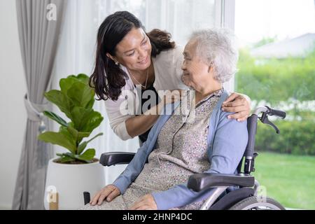 Pflegertochter helfen asiatischen älteren oder älteren Frau im Rollstuhl sitzen und tragen eine Gesichtsmaske zum Schutz der Sicherheitsinfektion Covid-19 Coronavirus. Stockfoto
