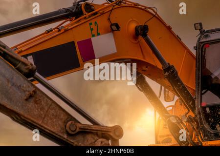 Nahaufnahme des hydraulischen Kolbenarms von schmutzigen Baggerlader auf der Baustelle. Gelber Bagger, der auf der Baustelle gegen den Abendhimmel geparkt ist. Baggermaschine. Hydraulikmaschinen. Bagger für Miete Geschäft. Stockfoto